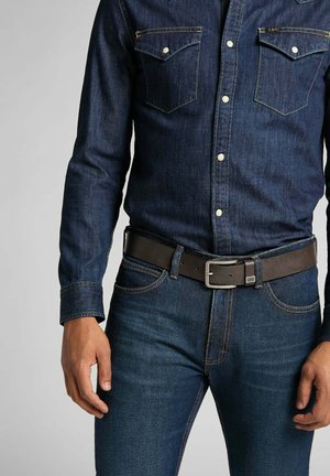Chemise en denim foncé avec un devant à boutons et des poches poitrine, associée à un jean bleu foncé et une ceinture en cuir marron avec une boucle en argent.