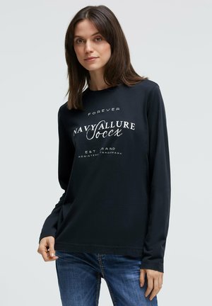 Schwarzes Langarmshirt mit weißem Text, darunter das Design "Navy Allure", Rundhalsausschnitt und weiche Stoffstruktur. Kombiniert mit blauen Jeans.