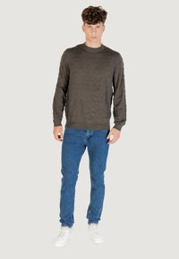 Dunkelgrüner Strickpullover mit Wellenmuster, Rundhalsausschnitt, kombiniert mit hellblauen Jeans und weißen Sneakers.