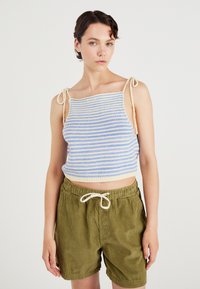 Raido tarjoiltu crop toppi vaaleansinisena ja kermaisen värisenä, jossa on säädettävät hihnat. Yhdistetty oliivinvihreisiin corduroy-shorteihin, joissa on joustava vyötärönauha.