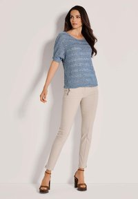 Lichtblauwe gebreide trui met korte mouwen, met een textuurpatroon; gecombineerd met beige strakke broek en bruine sandaaltjes met hak.