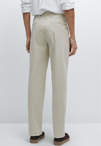Pantaloni beige in cotone con taglio dritto, dotati di tasche posteriori e una texture liscia, abbinati a scarpe casual marroni.