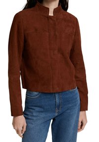Bruine suède gecropte jack met een hoge kraag, lange mouwen en subtiele stiksels, gecombineerd met blauwe spijkerbroeken.