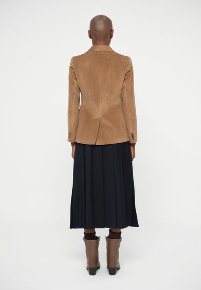 Rjav kordni blejzer z navpičnimi rebrinami, zadnji razporek in zapiranjem na gumbe. V kombinaciji s temno modrim krilom in rjavimi gležnjači.