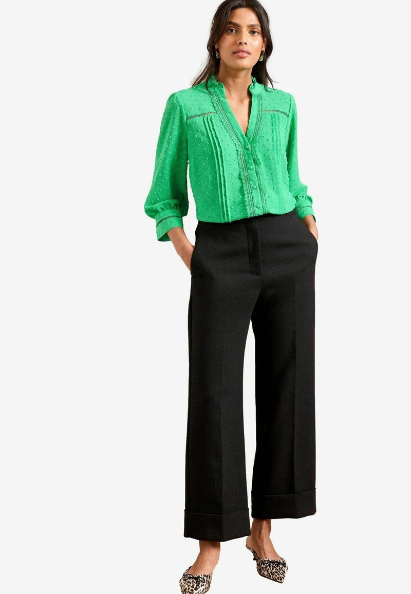 Blusa verde con texture, scollatura a V e bottoni, abbinata a pantaloni neri a vita alta e gamba larga, con scarpe ballerine in stampa leopardo.
