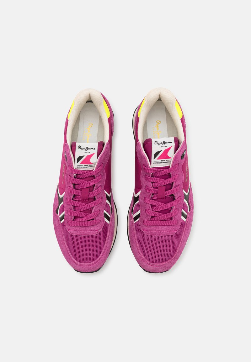 Lila Wildleder- und Mesh-Sneaker mit schwarz-weißen Akzenten, ausgestattet mit einem gepolsterten Kragen und flachen Schnürsenkeln. Gelbe Akzente in der Nähe der Ferse.