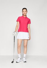 Rózsaszín pólóing gallérral, rövid ujjú, és egy fehér bővülő szoknya. Az egyik kezében golfütő, fehér sportcipőt és bokazoknit visel.