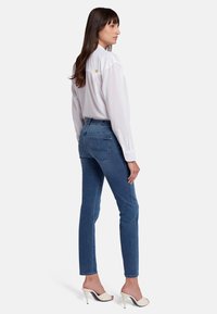 Camicia bianca a maniche lunghe con un dettaglio a stella sulla schiena, abbinata a jeans slim-fit blu e mule con tacco chiaro.