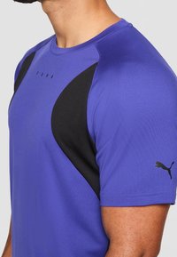 Camiseta deportiva violeta con detalles en negro. Presenta mangas cortas, textura suave y un pequeño logo en la manga derecha.