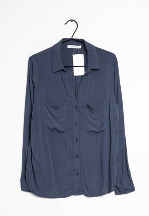 Marineblaue, langärmlige Hemdbluse mit Knöpfen und zwei Brusttaschen, hängt an einem schwarzen Kleiderbügel mit einem weißen Preisschild.