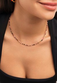 Collar de cuentas coloridas que presenta pequeñas cuentas redondas en rosa, negro, verde y amarillo. Se ve delicado con un diseño simple.