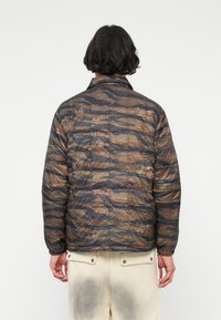 Quilted bomberjack in een camouflagepatroon, met tinten bruin en donkergroen. Elastische manchetten en zoom, lichte stoftextuur.