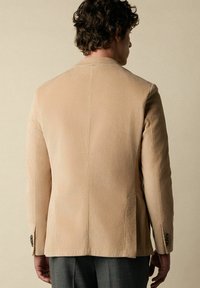 Beige korduroy blazer s oblekovým střihem, texturovanou tkaninou a strukturovanými rameny. Obsahuje knoflíky na manžetách a čistý design zad.