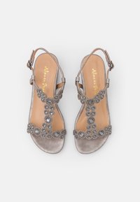 Hopeiset satiinisandaalit, joissa on litteä pohja. Koristeena kukkakuvioiset helmet ja solkisäie. Sileä beige sisäpohja. Avoin varvasosa.