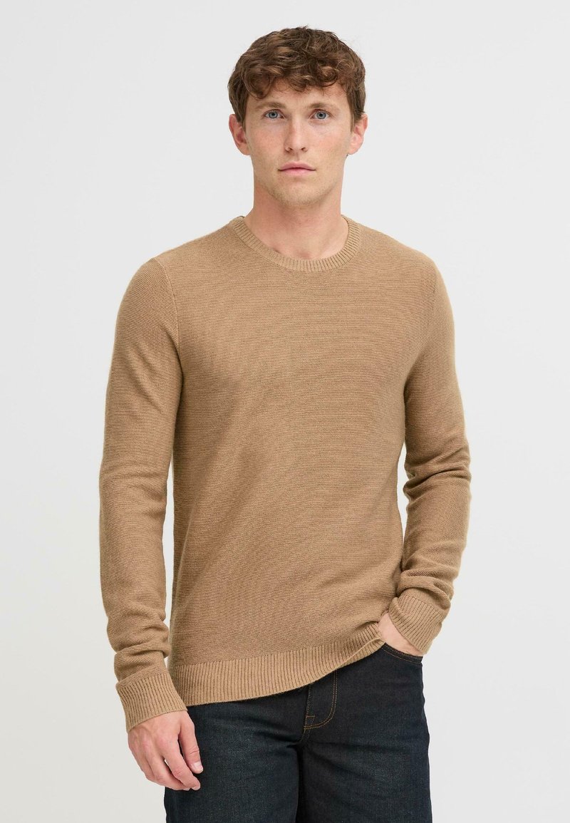 Suéter de punto beige con mangas largas y escote redondo. Presenta puños y dobladillo acanalados, confeccionado en una tela suave y texturizada.
