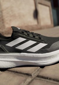 Scarpa sportiva nera e grigia con tre strisce bianche, tomaia texturizzata, soletta imbottita e finitura in tessuto liscio.