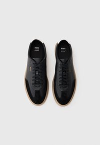 Zwarte leren sneakers met suède accenten, met een ronde neus, vetersluiting en een beige rubberen zool. Merkenlogo zichtbaar aan de binnenkant.