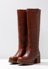 Bottes en cuir marron montantes avec une finition texturée, un bout rond et un talon épais. Présente des détails de couture et une languette à l'arrière.