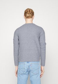 Maglione grigio a maglia con maniche lunghe e scollatura arrotondata, abbinato a jeans in denim azzurro chiaro, che mostrano un aspetto testurizzato e accogliente.