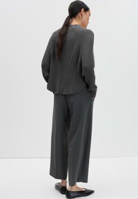 Maglione a coste grigio scuro con orlo arrotondato, abbinato a pantaloni grigio scuro a vestibilità morbida e ballerine nere, visto da dietro.