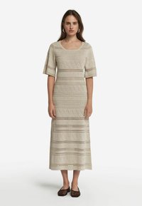 Virkat maxiklänning i ljusbeige med intrikata mönster och öppet hantverk, med korta ärmar och fyrkantig halsringning.