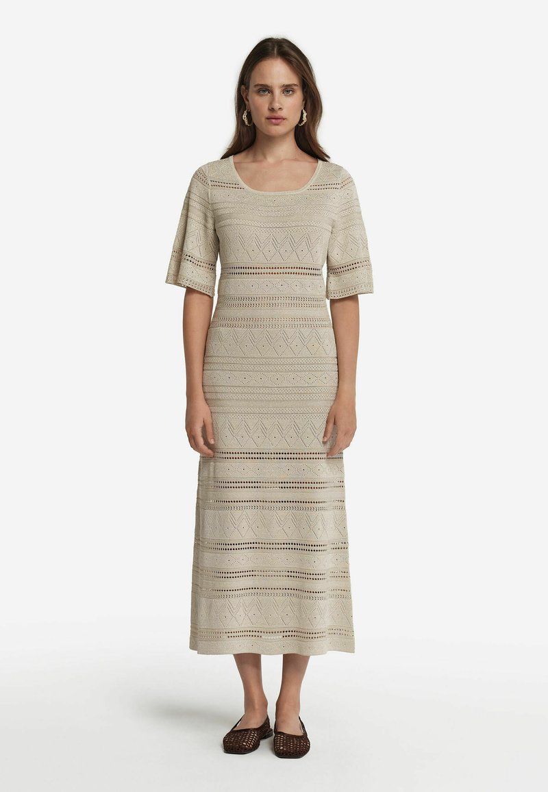 Virkat maxiklänning i ljusbeige med intrikata mönster och öppet hantverk, med korta ärmar och fyrkantig halsringning.