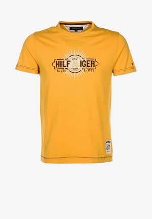 T-shirt gialla a maniche corte con la scritta "Hilfiger New York Reg. USA Est. 1985" e una toppa grafica bianca sulla parte inferiore anteriore.