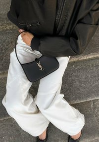 Mustassa nahkabägissä on kultainen YSL-logo, se on jämäkkärakenteinen ja siinä on ohut hihna. Bägiä on yhdistetty valkoisiin leveälahkeisiin housuihin ja mustaan bomber-takkiin.