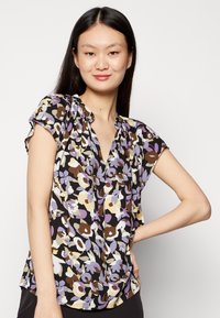 Blusa floral em tons de roxo, castanho e creme. Mangas curtas com decote plissado e um corte solto. Tecido leve e suave.