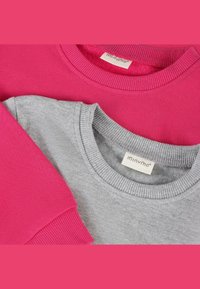 Sudaderas de cuello redondo en tonos rosa y gris, dobladas y con puños y cuellos acanalados, cada una mostrando una etiqueta de marca blanca que dice "minymo."
