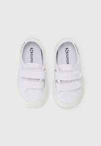 Zapatos de lona blancos con dos correas de velcro, punta redonda y suela de goma. Logo de la marca impreso en la plantilla. Diseño simple y ligero.