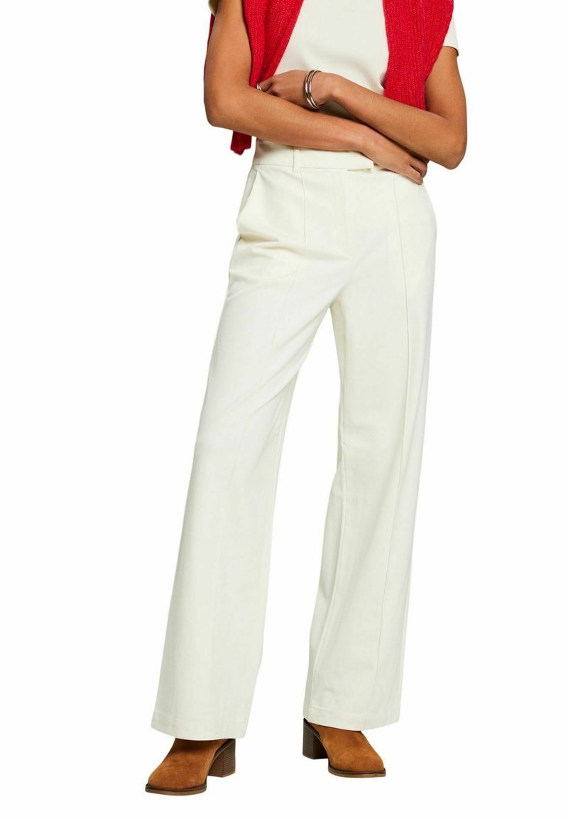 Pantalon blanc à jambes larges avec une coupe ajustée, doté de plis à l'avant, d'une texture lisse et de poches latérales, associé à des bottines marron à talons blocs.