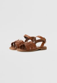 Brune lær sandaler med udskæringsdesign, justerbar ankelrem, flad sål og glat overflade. Har et minimalistisk æstetik.