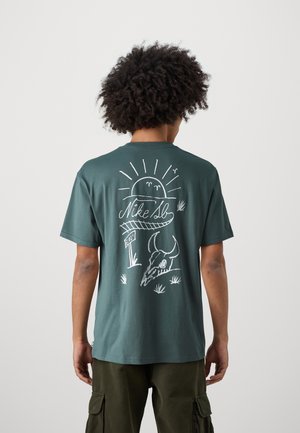 Grünes Baumwoll-T-Shirt mit kurzen Ärmeln, das ein weißes grafisches Design mit einer Sonne, einem Totenkopf und Text auf dem Rücken zeigt. Lässiger Schnitt mit rundem Hals.