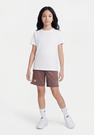 Ung person iført hvid t-shirt, brune sportsshorts med logoer, hvide Nike-strømper og hvide sneakers på en helt hvid baggrund.