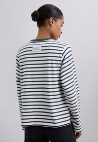 Camisa de manga larga a rayas en blanco y gris oscuro, con cuello redondo y etiqueta de logo en la parte posterior. Tejido de algodón suave con un ajuste holgado.