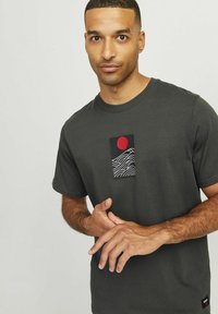 Dark gray t-shirt with short sleeves. Features a graphic design of red sun and white wave patterns on a black rectangle. Cotton material.