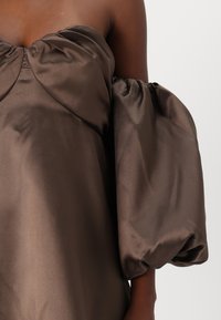 Barna selyem anyagú, váll nélküli felső, plisszírozott mellrésszel és túlméretezett puff ujjakkal, sima, enyhén fényes textúrával.