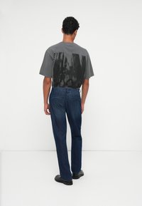 Grå grafisk t-skjorte med et uskarpt design på baksiden, kombinert med mørkeblå denimjeans og svarte sko. En enkel, avslappet antrekk.