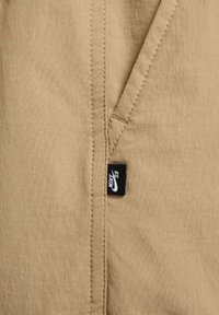 Beżowa tkanina o gładkiej fakturze, z przeszyciem i małą czarną metką Nike w dolnym rogu.