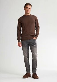 Ruskea neulepaita, harmaat farkut ja ruskeat saappaat. Neulepaidassa on pyöreä pääntie ja pitkät hihat, ja farkuissa on haalistunut viimeistely.