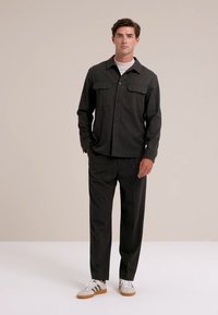 Fekete gombos ing két mellzsebbel, illesztett nadrággal és barna árnyalatú fehér sportcipővel párosítva. Egyszerű, szabott dizájn.