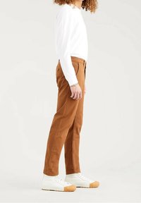 Bruna bomullsbukser med rak passform, i kombination med en vit långärmad skjorta och vita sneakers med en beige gummisula.