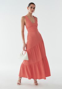 Koronowy bezrękawnik z warstwowym krojem, teksturowanym materiałem i głębokim dekoltem w kształcie litery V. W zestawie z białą torebką na ramię z okrągłym uchwytem.