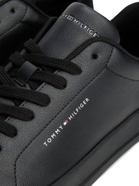 Ténis pretos em pele com superfície texturizada, atacadores pretos e detalhe da marca "TOMMY HILFIGER" em branco na lateral. Design suave.