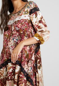 Sukienka w kwiaty z okrągłym dekoltem, rękawami o długości 3/4 oraz mieszanką kolorów bordowego, kremowego i czarnego. Lekka, teksturowana tkanina.