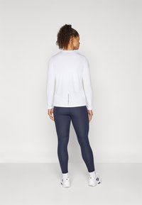 Hvit langermet treningstopp med detalj i ryggen, kombinert med marineblå leggings. Smooth tekstur, tett passform, egnet for sportsaktiviteter.