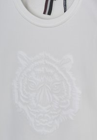 T-shirt bianco con un design in rilievo raffigurante la faccia di una tigre. Il materiale presenta una texture liscia e un collo girocollo con un'etichetta interna a contrasto.