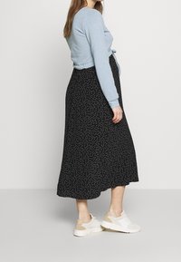 Světle modrý zkrácený svetr s dlouhými rukávy v kombinaci s midi sukní s černými puntíky. Neformální bílé tenisky s béžovými akcenty.