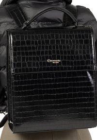 Sac à dos en simili cuir noir avec une texture crocodile brillante, forme structurée et une poignée supérieure. Détails du logo doré.